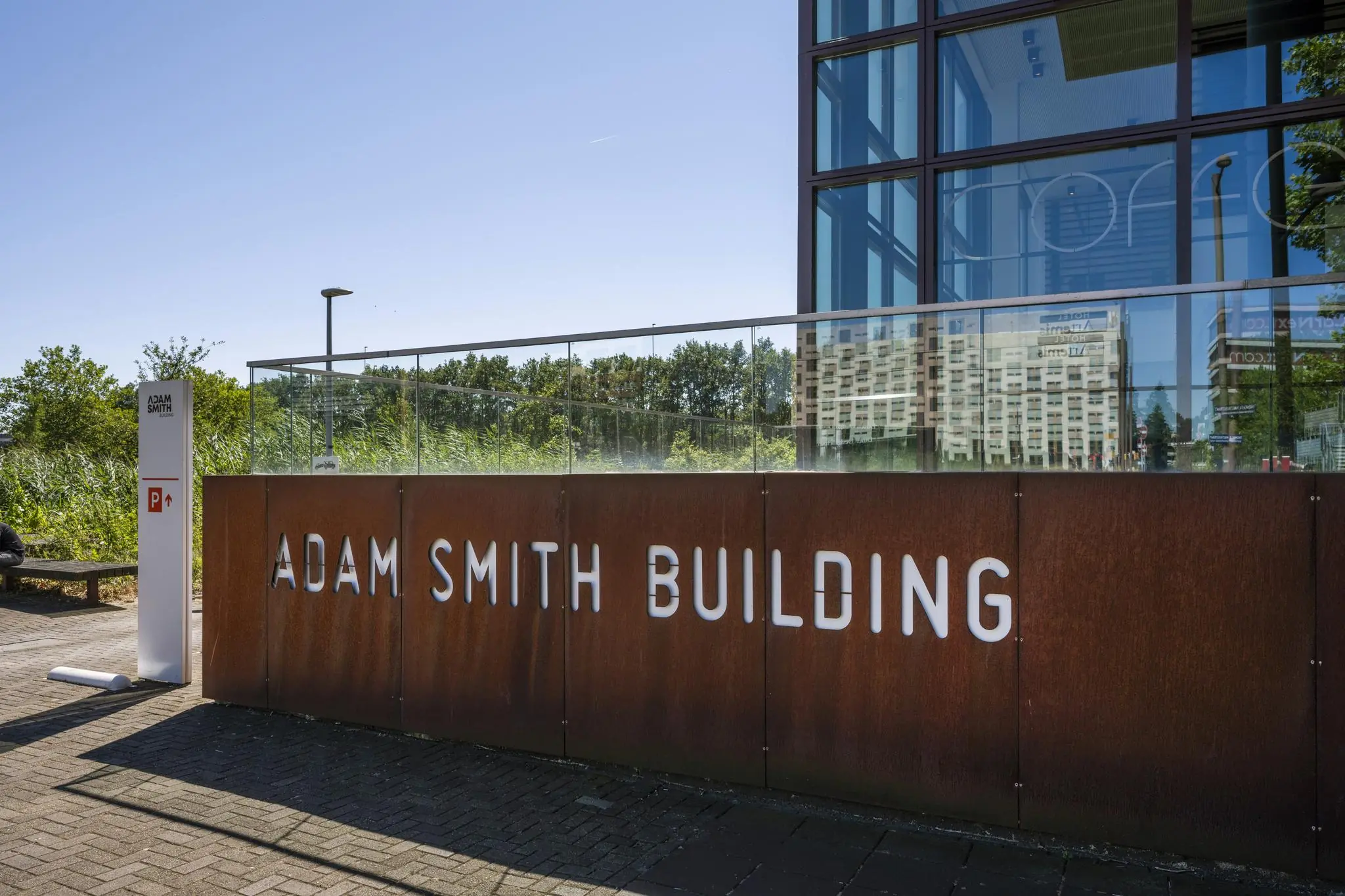 Vooraanzicht van het Adam Smith Building aan de Thomas R. Malthusstraat met moderne gevel en naambord.