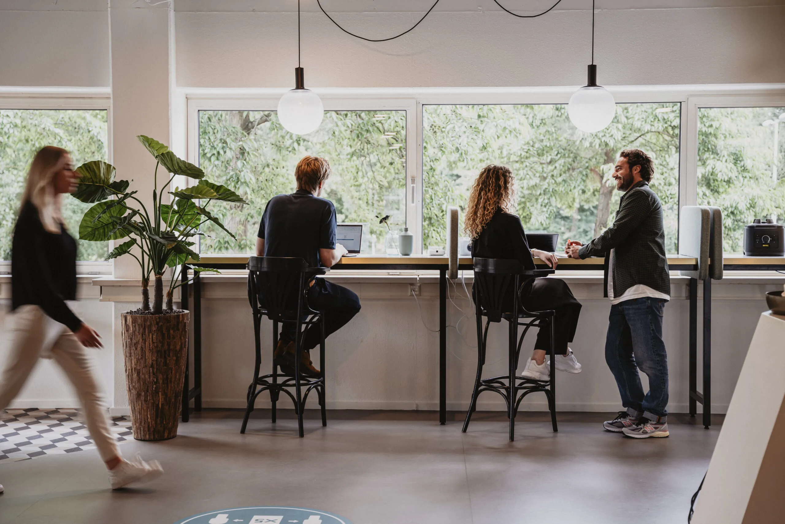 Mensen werken en overleggen bij een hoge werktafel met laptops in een moderne, lichte ruimte in HNK Amsterdam Schinkel.