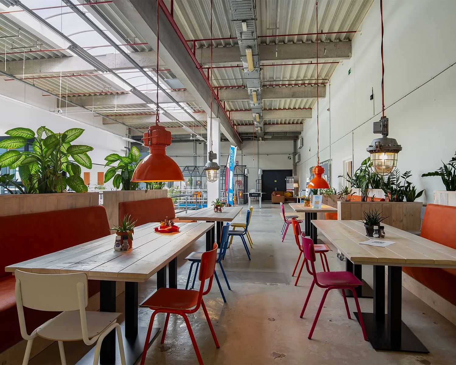 Moderne en kleurrijke kantoorruimte aan de Bolderweg 2 in Almere met lange houten tafels, felgekleurde stoelen, oranje hanglampen en veel groen.