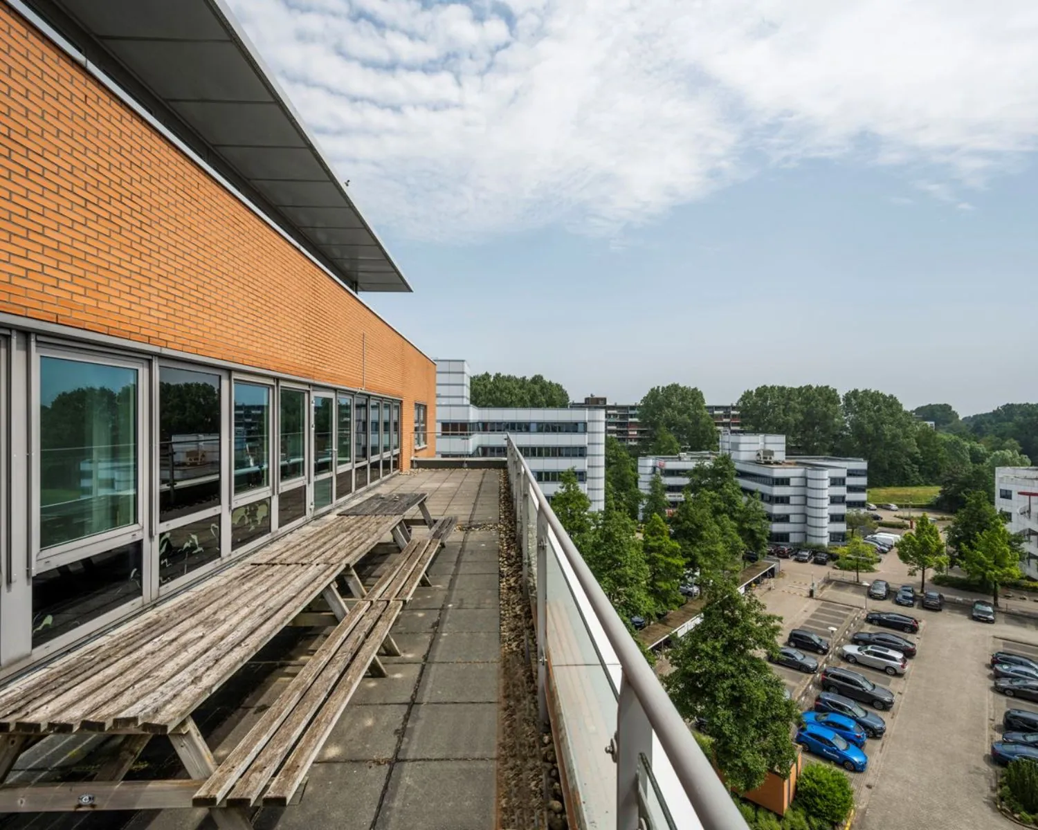 Dakterras met houten picknicktafels bij kantoorruimte Entrada 300 in Amsterdam, met uitzicht op parkeerterrein en omliggende kantoorgebouwen.