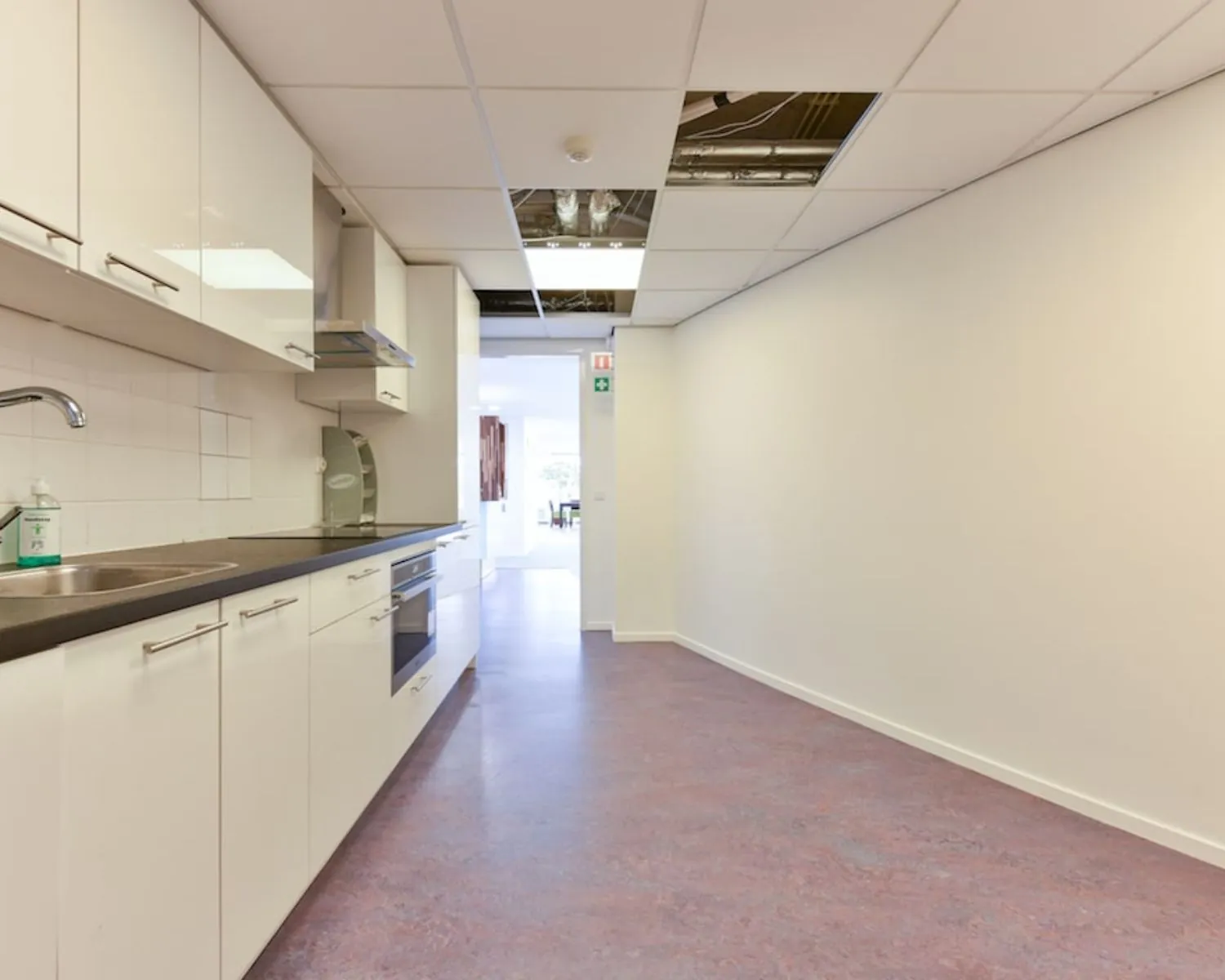 Keukenruimte in een kantoor aan de Treubstraat 1 in Rijswijk met witte kasten, een ingebouwde oven en een systeemplafond met open panelen.