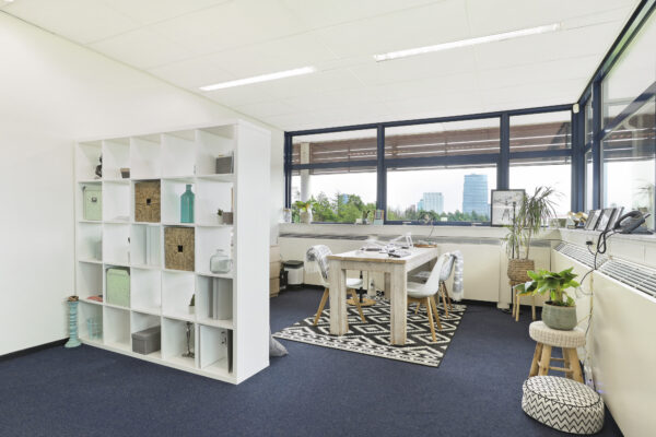 Een lichte, moderne kantoorunit met een houten tafel, open plankenkast en grote ramen.