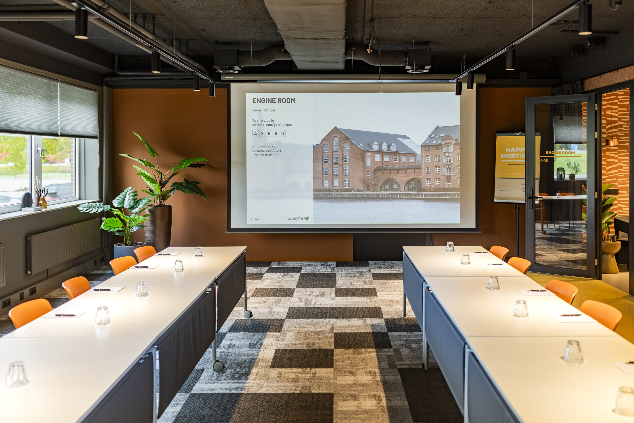 Een moderne vergaderruimte met een projectiescherm en tafels die zijn ingericht voor een bijeenkomst.