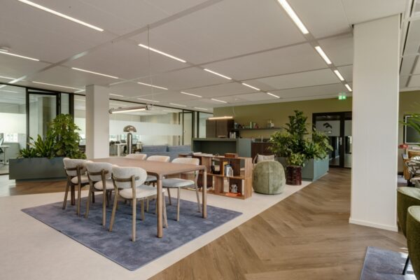 Moderne kantoorruimte met een houten tafel en comfortabele stoelen, omringd door groene planten en glazen wanden.