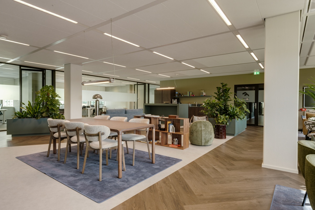 Moderne kantoorruimte met een houten tafel en comfortabele stoelen, omringd door groene planten en glazen wanden.