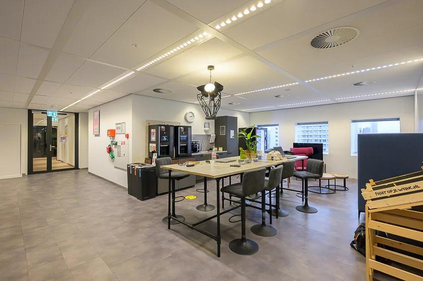 Moderne kantoorpantry met hoge tafel, barkrukken, koffieapparaten en uitzicht op de stad aan de Weena.