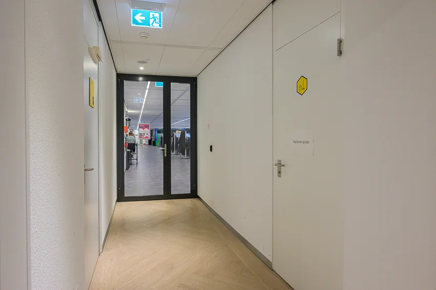 Hal met lichte houten vloer en witte deuren die leidt naar een winkelruimte aan de Weena.