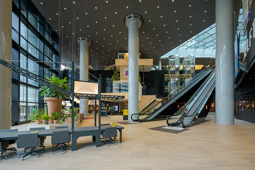 Moderne, ruime lobby van het kantoorgebouw aan het Weena met roltrappen, glazen liften en grote kolommen.