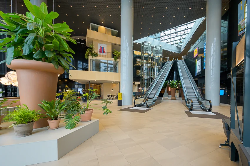 Moderne en ruime entreehal van kantoorgebouw Weena met roltrappen, glazen liften en grote planten.