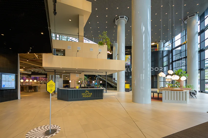 Moderne, lichte ontvangsthal van gebouw De Delftse Poort in Rotterdam met hoge plafonds, grote zuilen en een informatiebalie.