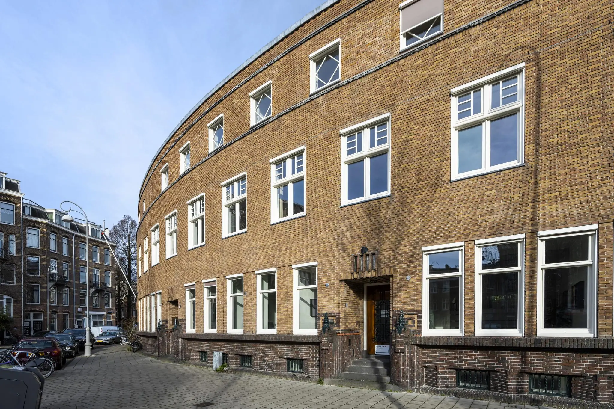 Gebogen bakstenen woongebouw aan het Concertgebouwplein in Amsterdam met witte raamkozijnen en een ronde gevel.