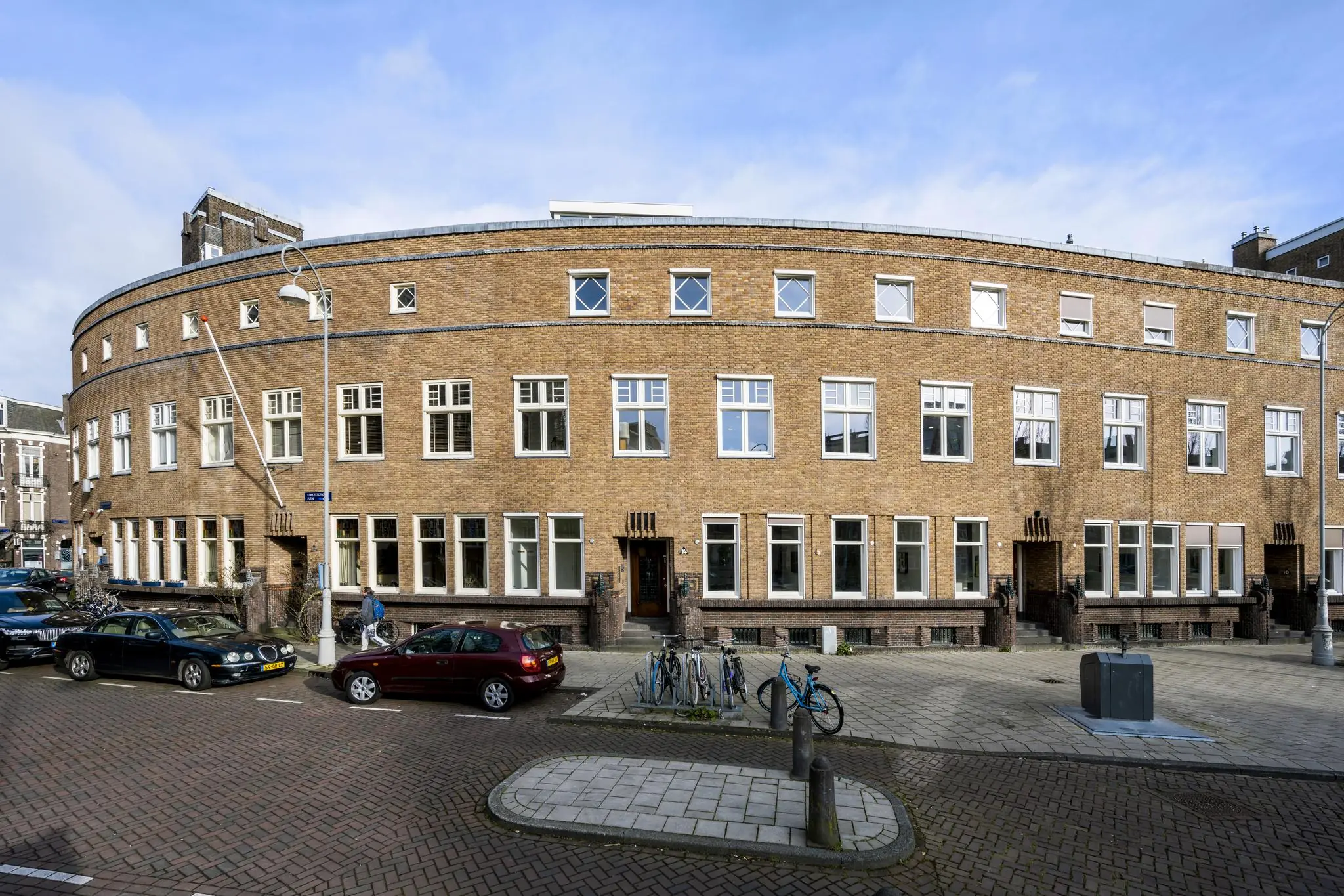 Gebogen woongebouw in Amsterdam aan het Concertgebouwplein met bakstenen gevel en witte kozijnen.