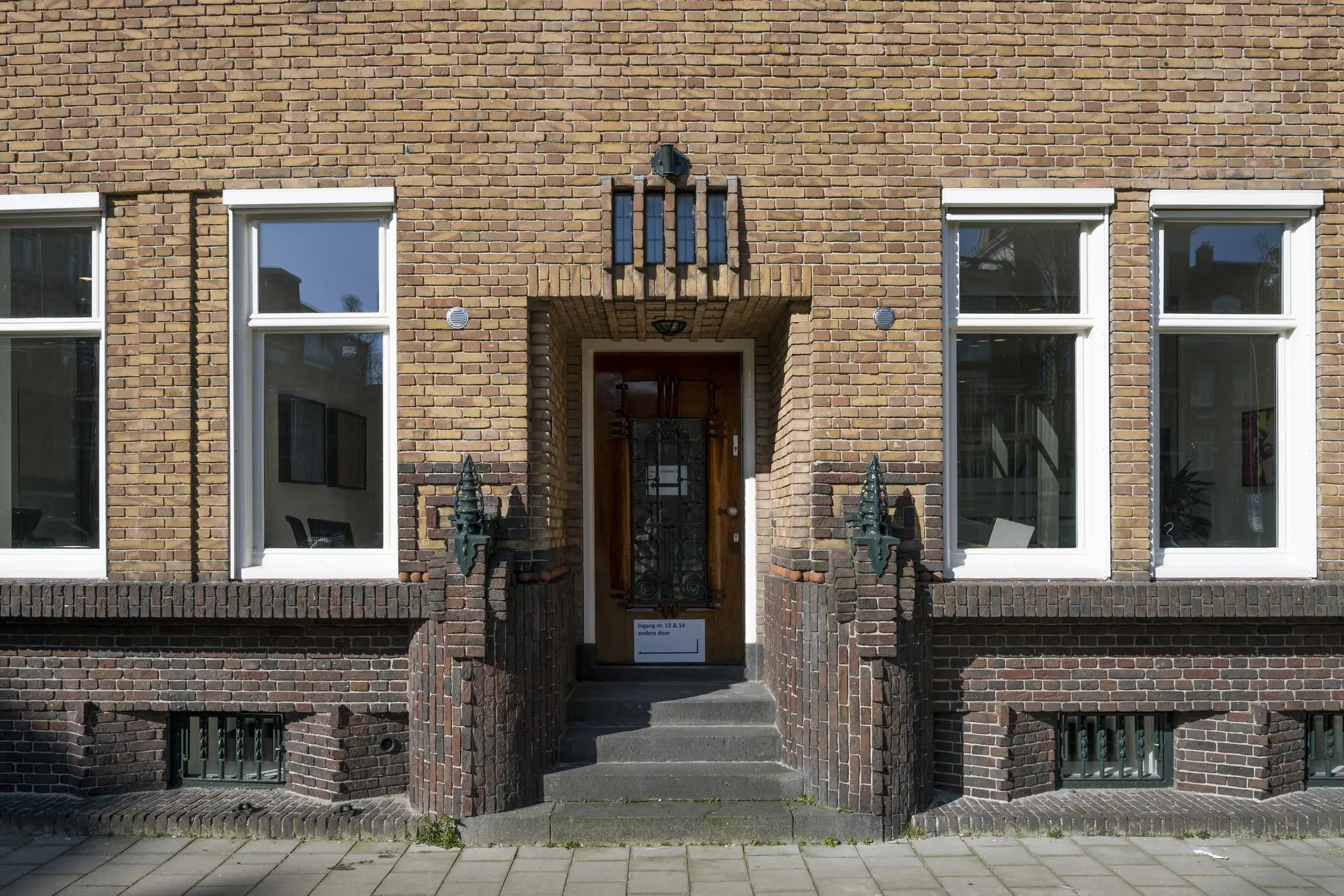 Voordeur met trap en symmetrische ramen van een bakstenen woning aan het Concertgebouwplein in Amsterdam.