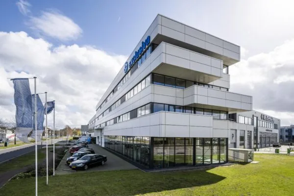 Modern kantoorgebouw van Exclusiva aan de Dynamostraat met geparkeerde auto’s en vlaggen op de voorgrond.