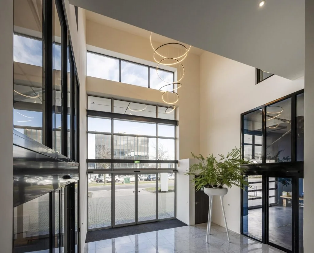 Moderne entreehal van een kantoorpand aan de Dynamostraat met hoge ramen, glazen deuren en een hangende designlamp.