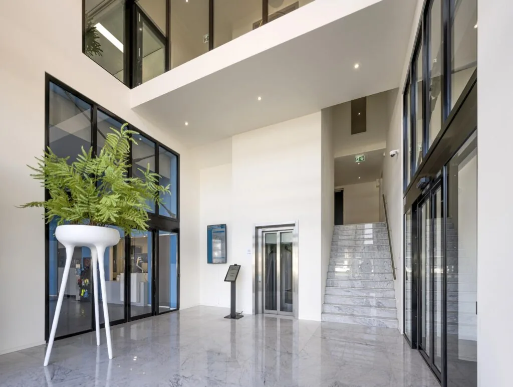 Moderne entreehal aan de Dynamostraat met marmeren vloer, glazen gevel, lift, trap en een grote design plantenbak.