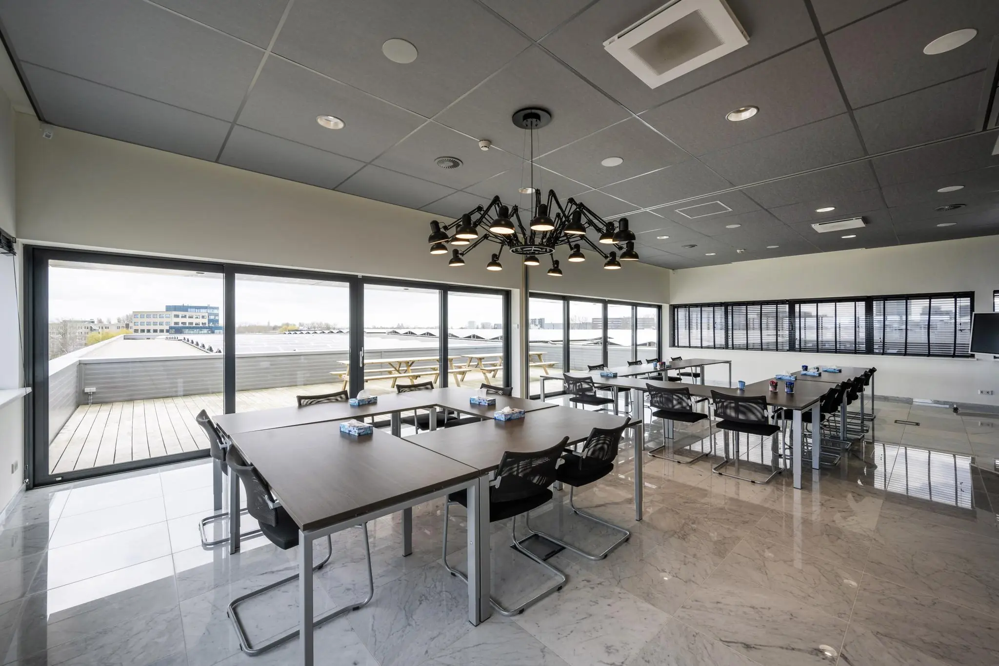 Moderne vergaderruimte aan de Dynamostraat met grote ramen, industriële verlichting en uitzicht op een dakterras.