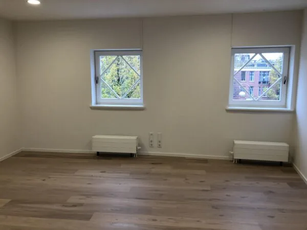 Lichte, lege kamer met houten vloer en twee ramen met uitzicht op het Concertgebouwplein in Amsterdam.