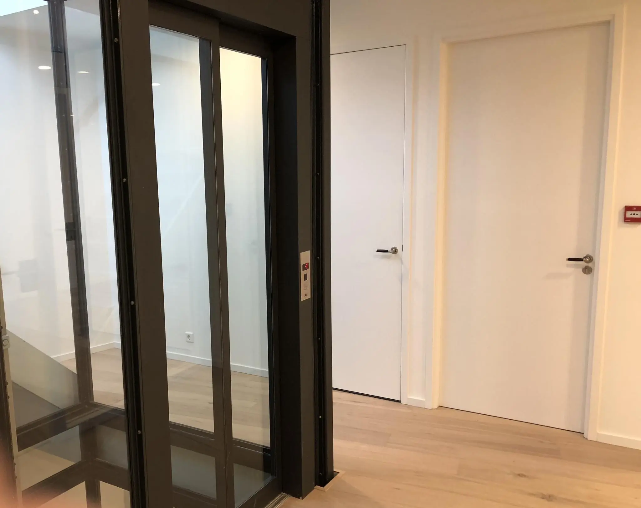 Glazen lift en twee witte deuren in een modern interieur op Concertgebouwplein.