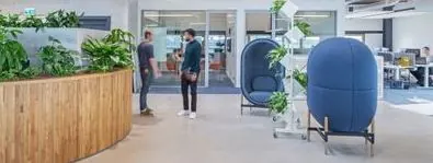 Moderne kantoorlobby aan de Ptolemaeuslaan met planten, zitpods en mensen in gesprek.