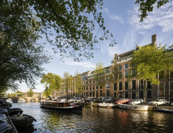Zicht op de Herengracht in Amsterdam met grachtenpand Herengracht 168, boten op het water en bomen langs de kade.