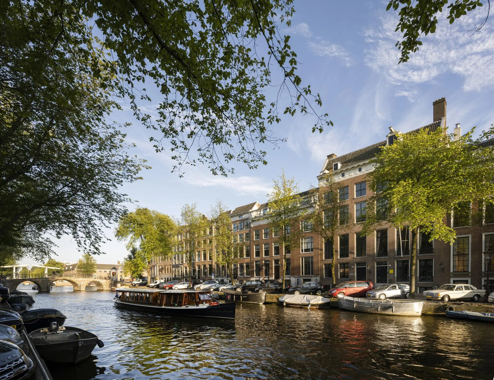 Zicht op de Herengracht in Amsterdam met grachtenpand Herengracht 168, boten op het water en bomen langs de kade.