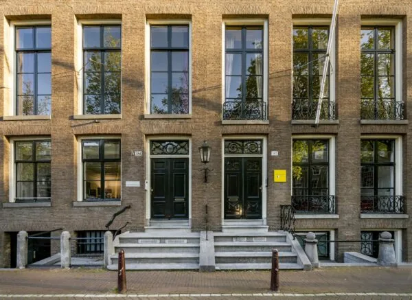 Twee klassieke grachtenpandgevels aan de Herengracht in Amsterdam met hoge ramen en zwartgelakte voordeuren.