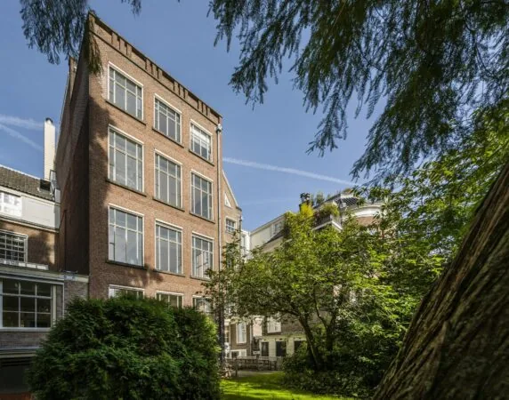 Achtergevel van een klassiek Amsterdams grachtenpand aan de Herengracht, omgeven door een groene tuin.