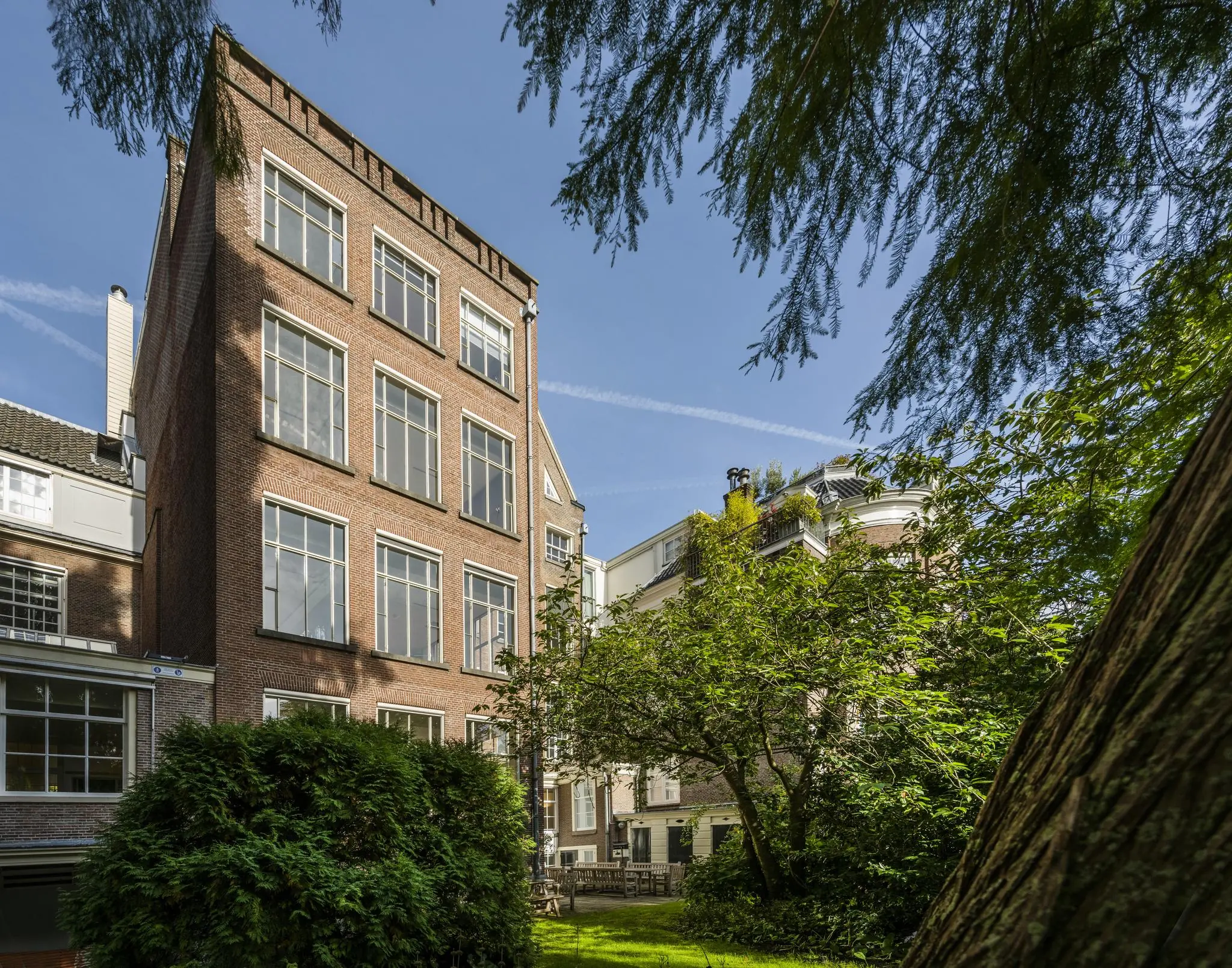 Achtergevel van een klassiek Amsterdams grachtenpand aan de Herengracht, omgeven door een groene tuin.