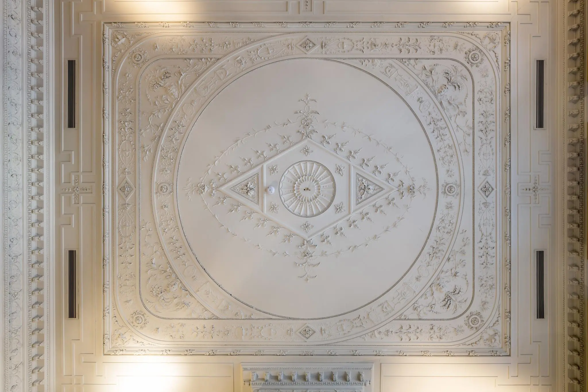 Sierlijk gedecoreerd plafond met symmetrische ornamenten en florale motieven in een historisch pand aan de Herengracht.