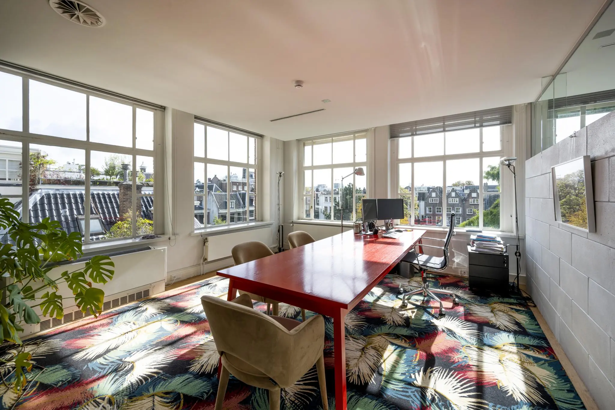 Modern kantoor met grote ramen aan de Herengracht, met uitzicht op Amsterdamse gevels en een kleurrijk tapijt.