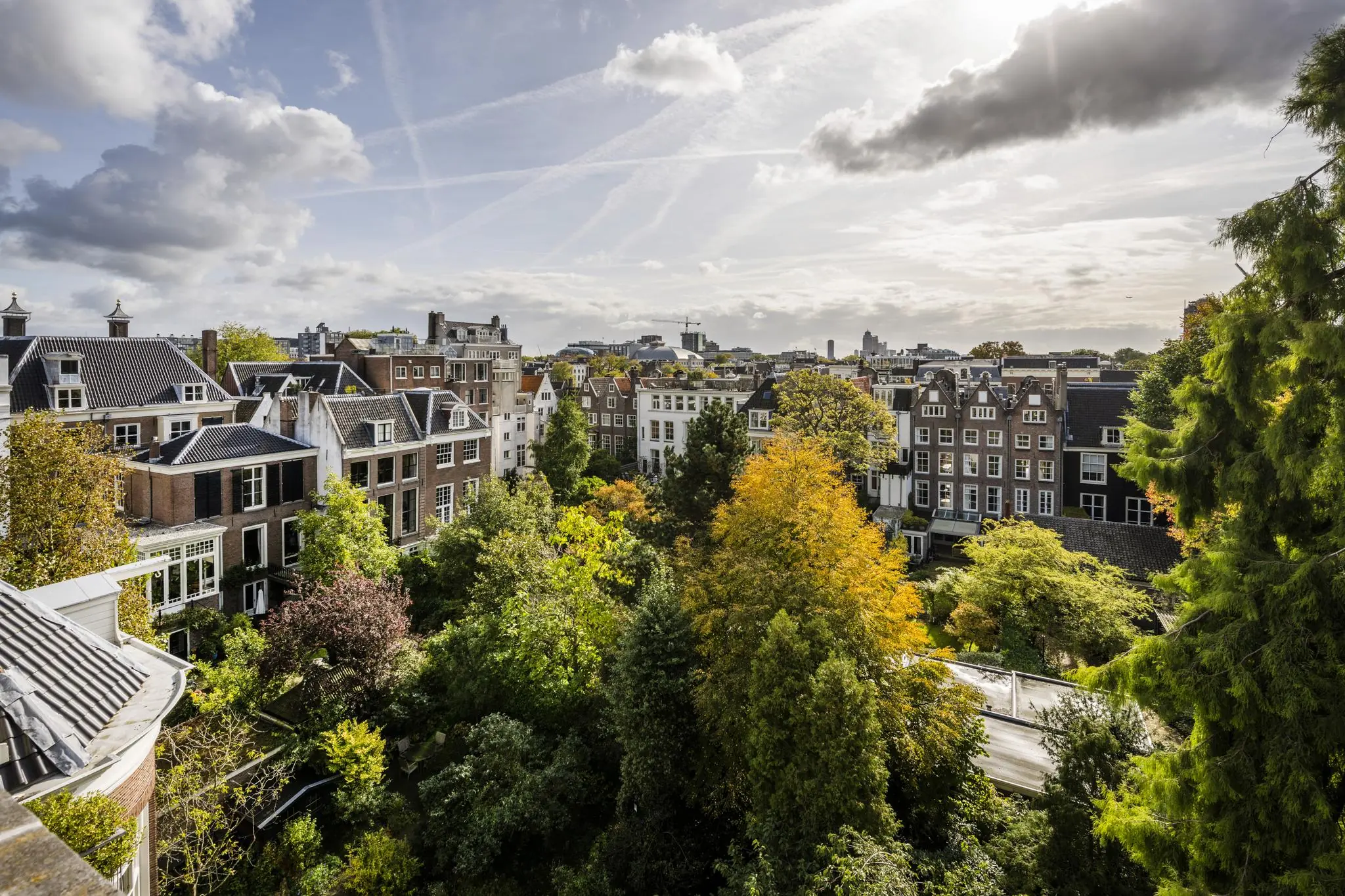 Uitzicht op klassieke grachtenpanden aan de Herengracht in Amsterdam, omringd door weelderige stadstuinen en herfstkleuren.