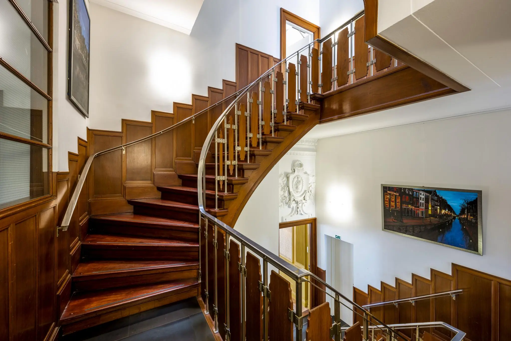 Trap met houten betimmering en leuning van metaal in een stijlvol interieur aan de Herengracht, met een foto van Amsterdam aan de muur.