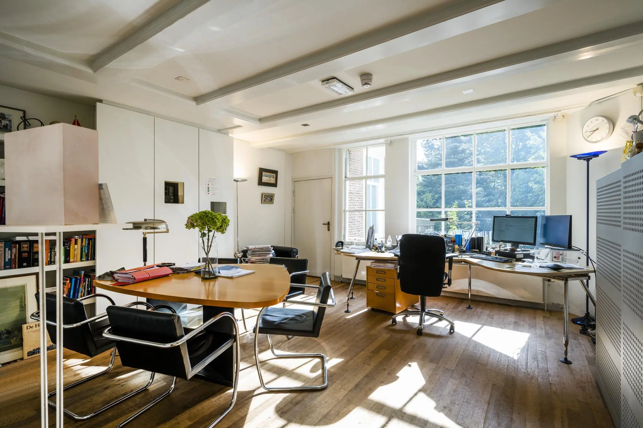 Licht en modern kantoor aan de Herengracht met bureau, vergadertafel en grote ramen met uitzicht op groen.