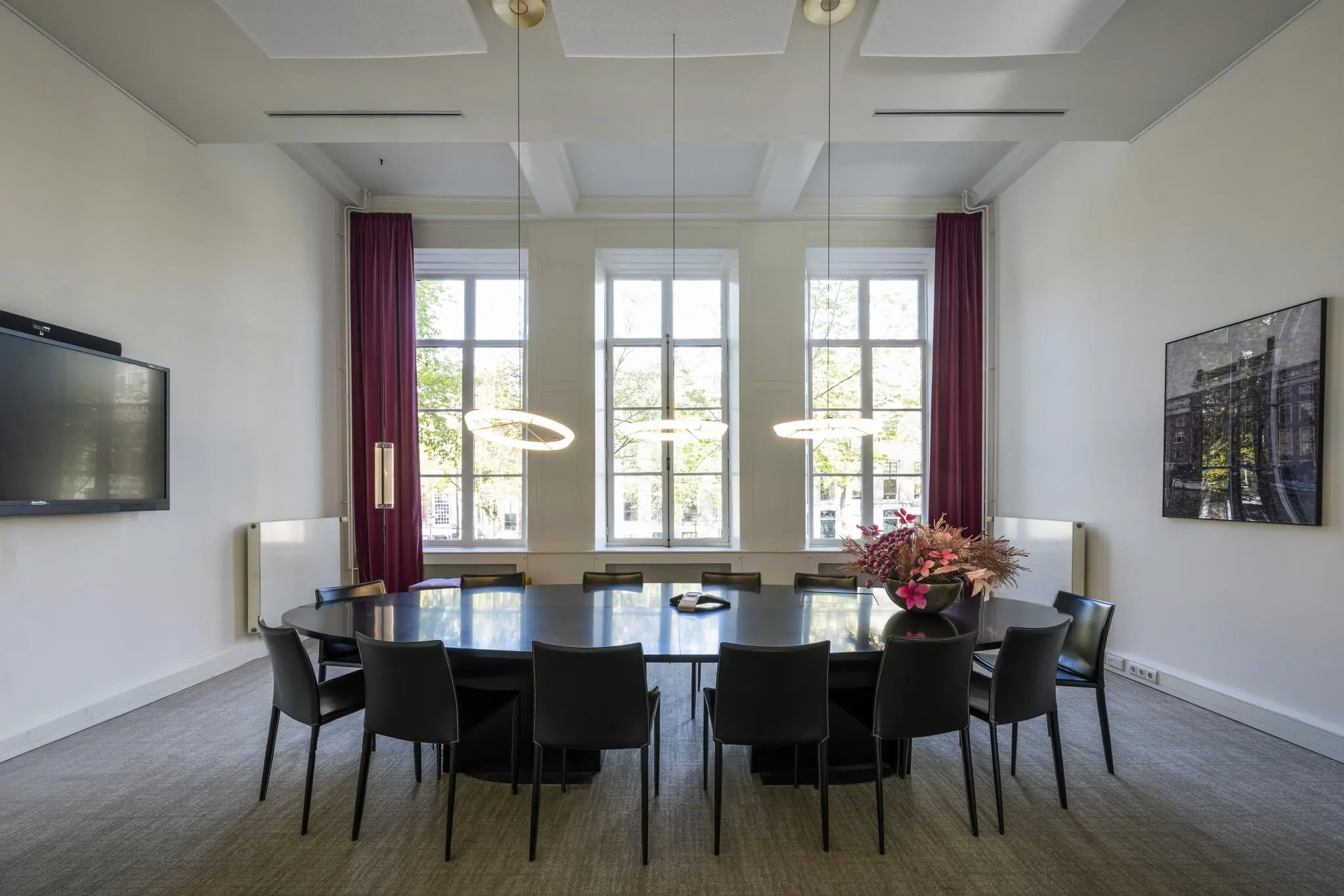 Vergaderruimte aan de Herengracht met grote ovale tafel, moderne verlichting en hoge ramen met uitzicht op de gracht.