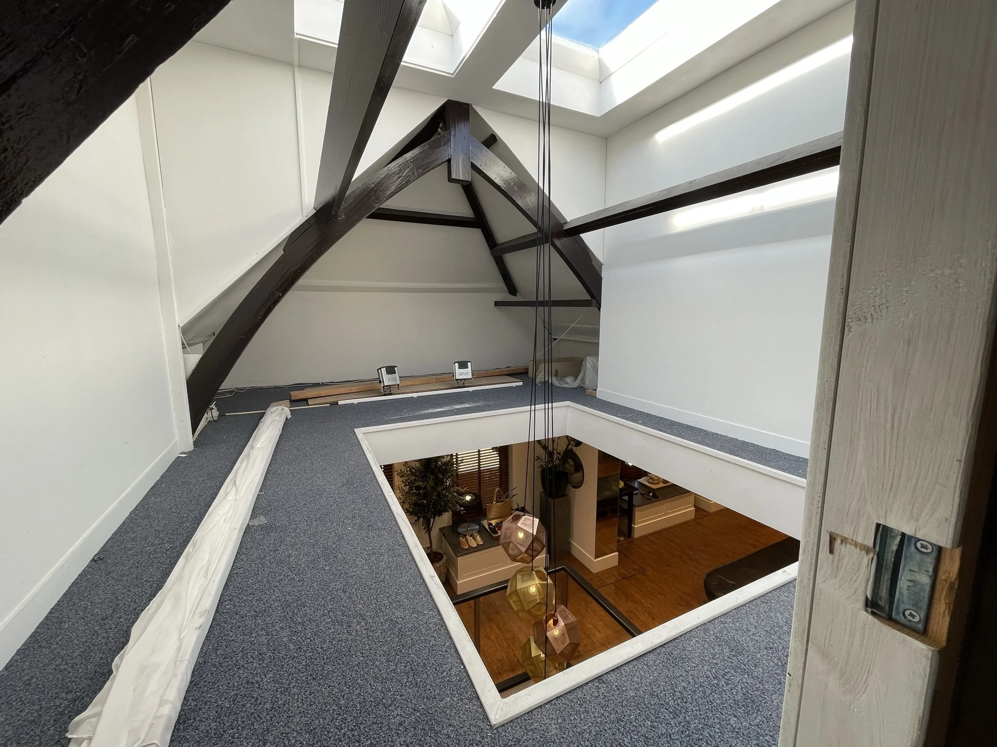Zolderruimte met donkerhouten balken, tapijt en een open vide met zicht op de woonruimte beneden in een pand aan de Molendijk.