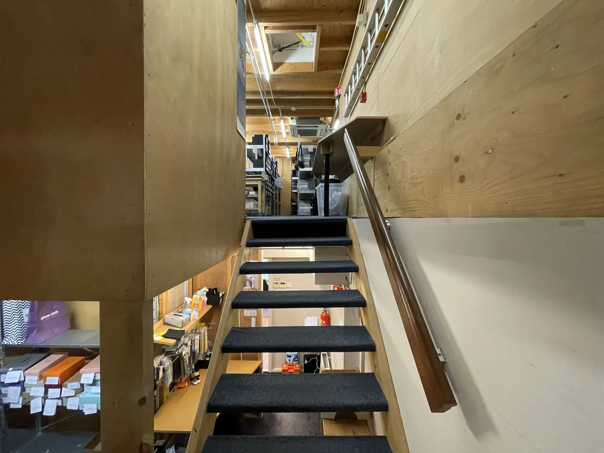 Trap met zwarte treden en houten leuning in een magazijnachtige ruimte aan de Molendijk.