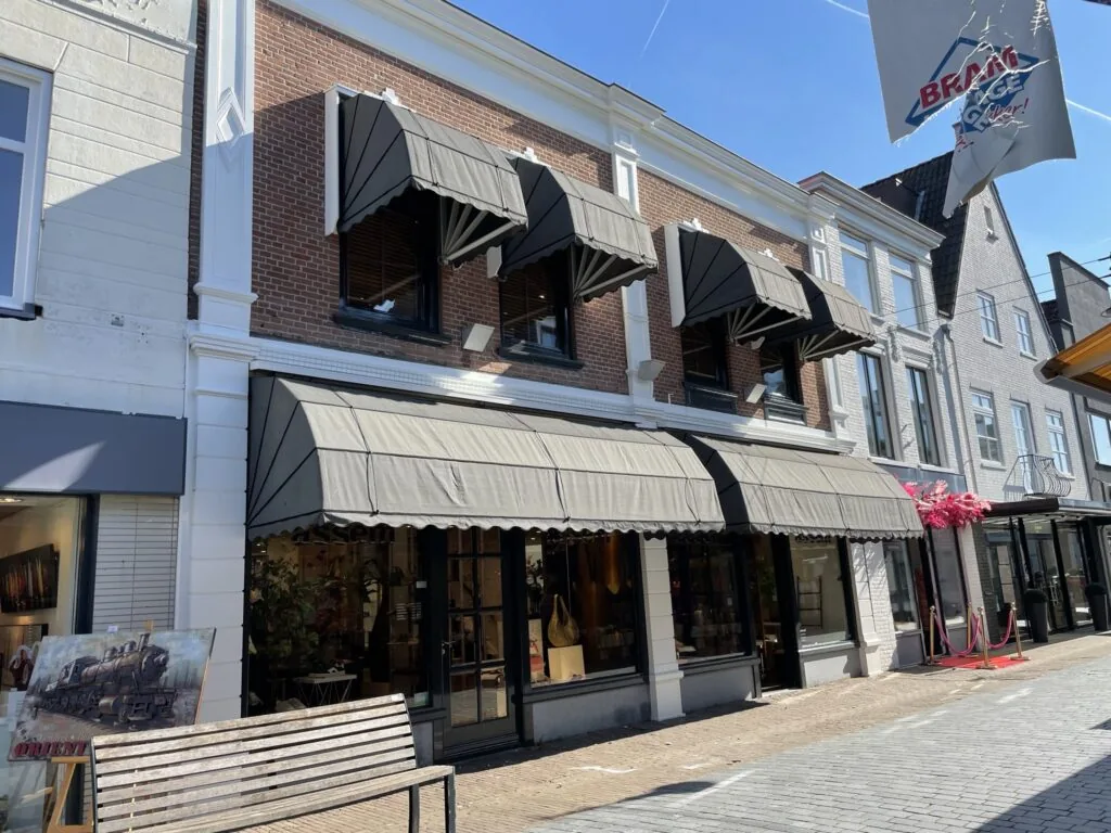 Winkelpand aan de Molendijk met zwarte zonneschermen en etalage op een zonnige dag.