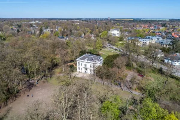 Luchtfoto van een wit herenhuis aan de Utrechtseweg in Arnhem, omgeven door bomen en stadsbebouwing.