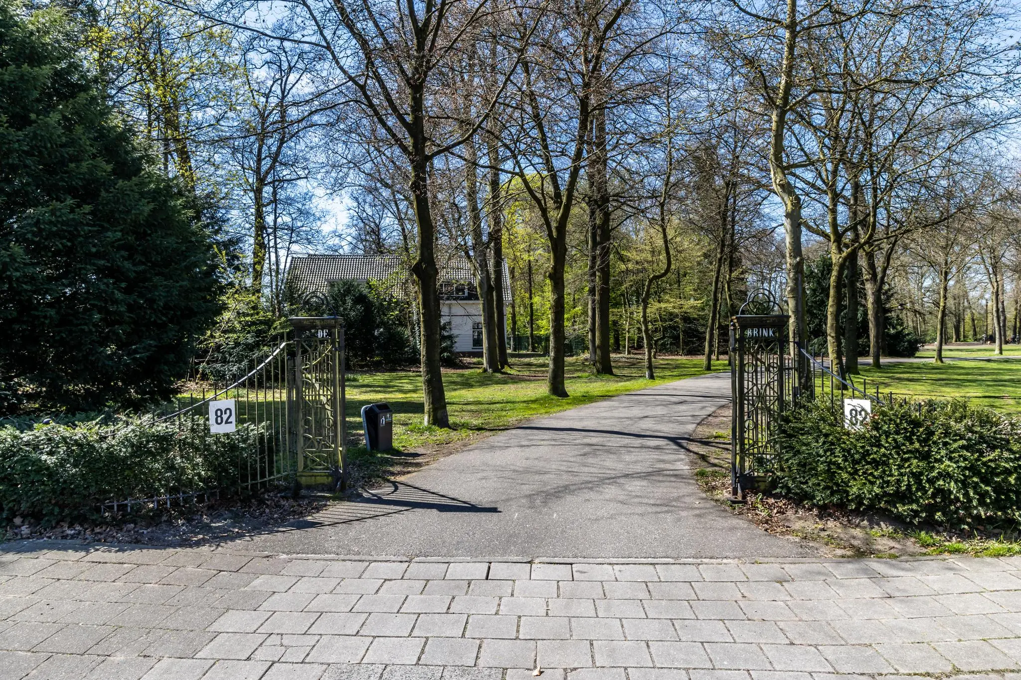 Oprit met sierhek en huisnummer 82 aan de Utrechtseweg, omgeven door bomen en groen.