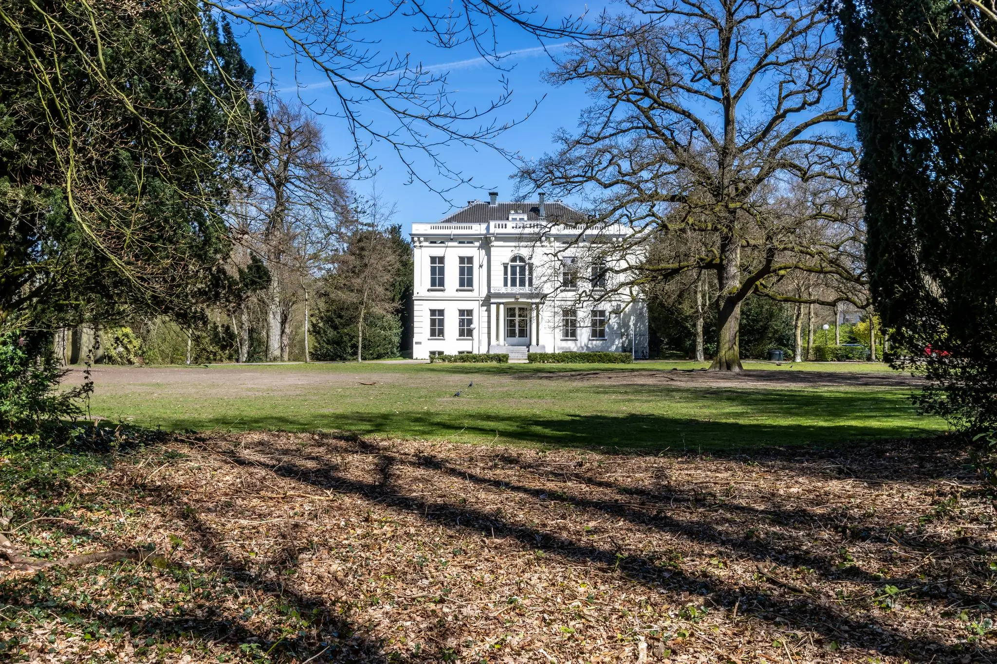 Wit herenhuis aan de Utrechtseweg omringd door bomen en een groot grasveld.