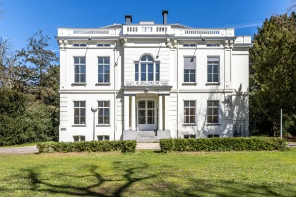 Wit klassiek herenhuis aan de Utrechtseweg, omringd door groen en badend in zonlicht.