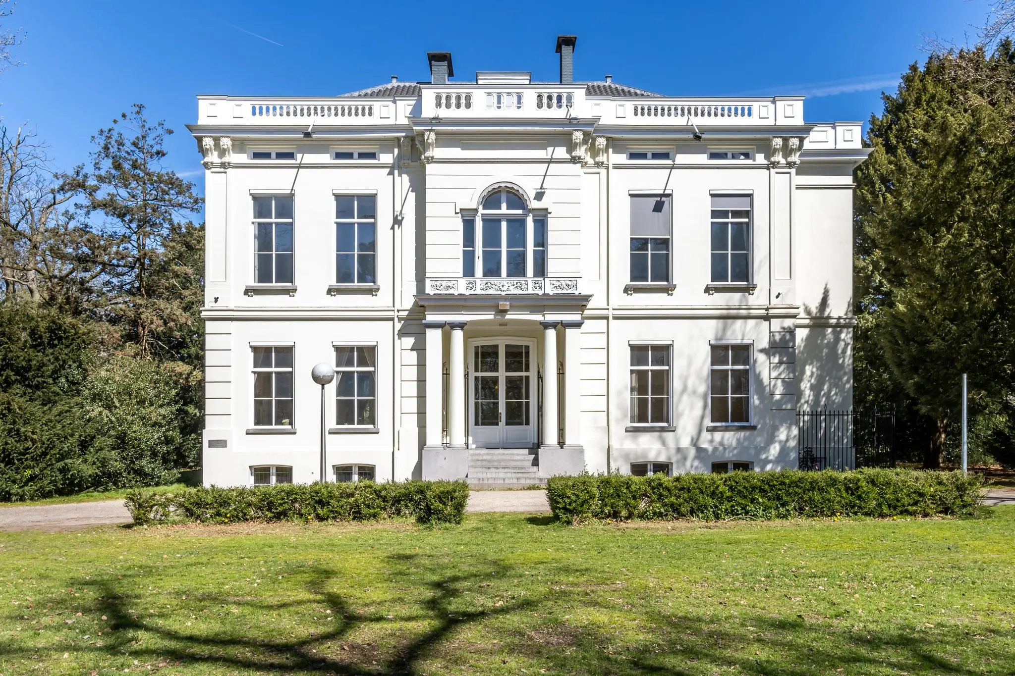 Wit klassiek herenhuis aan de Utrechtseweg, omringd door groen en badend in zonlicht.