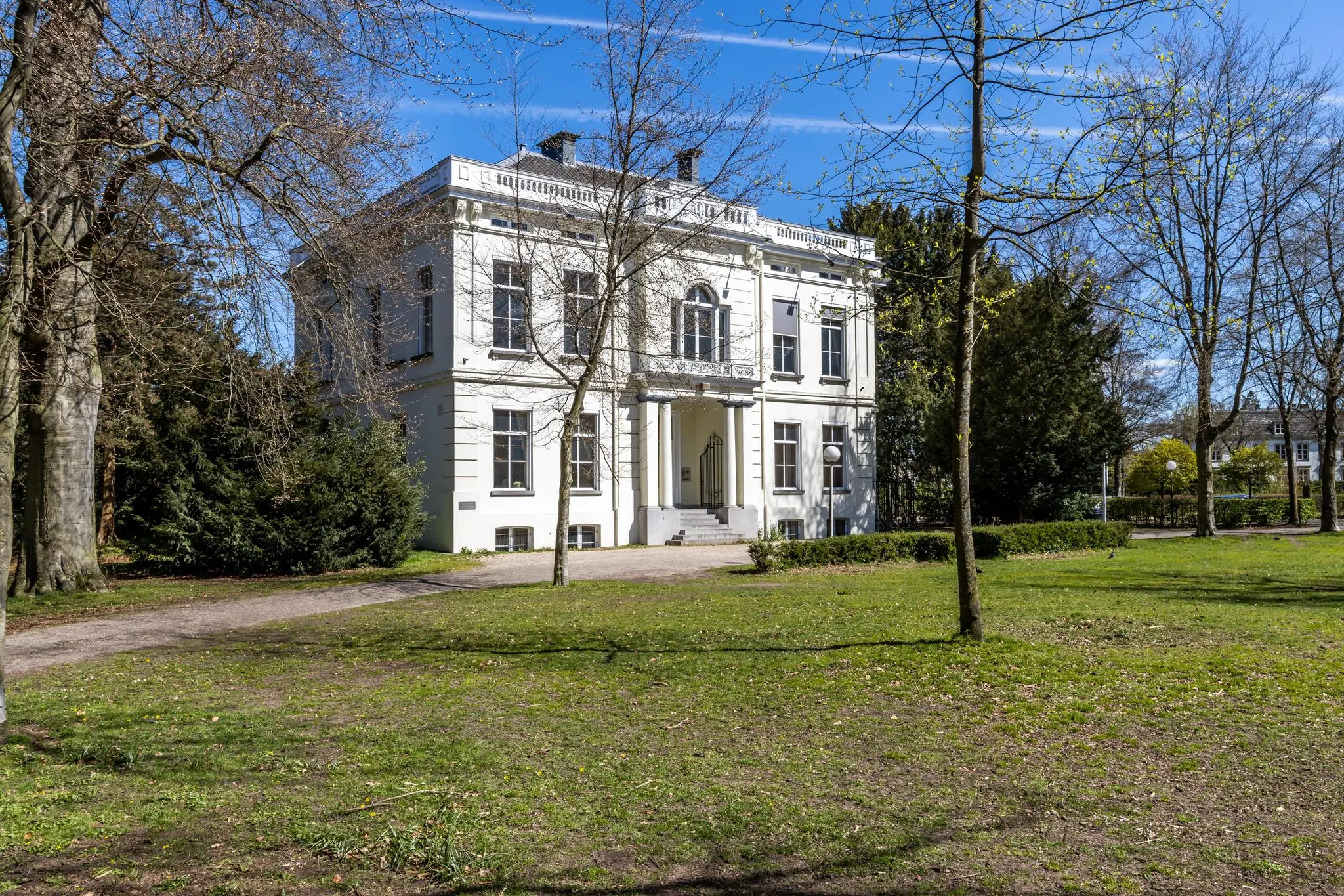 Wit herenhuis aan de Utrechtseweg in Arnhem, omgeven door een groen park met bomen.