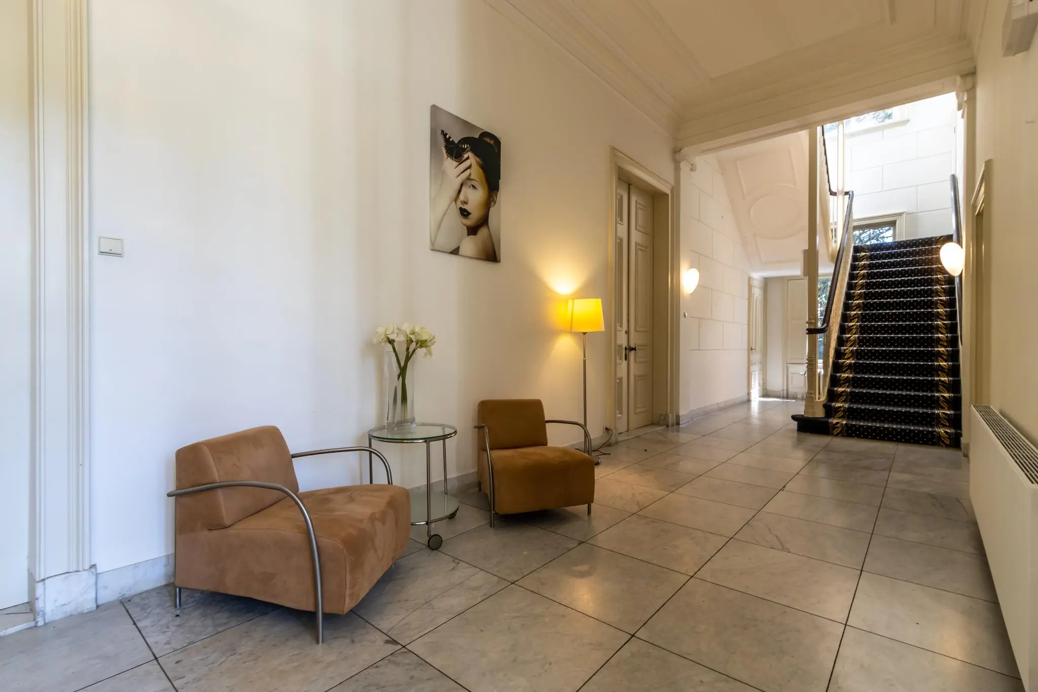 Stijlvolle hal aan de Utrechtseweg met marmeren vloer, zitgedeelte, kunst aan de muur en een trap met zwart tapijt.