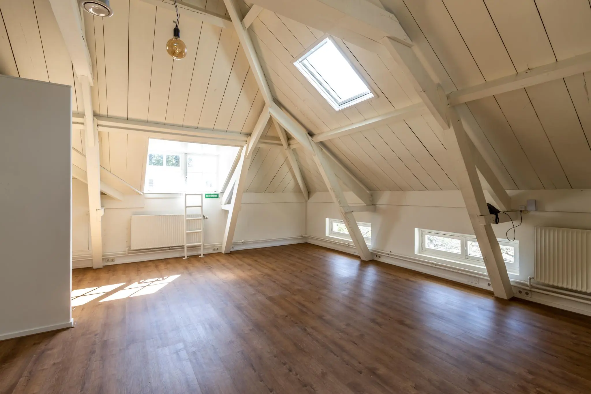 Zolderruimte met houten vloer, witgeschilderde balken en meerdere ramen aan de Utrechtseweg.
