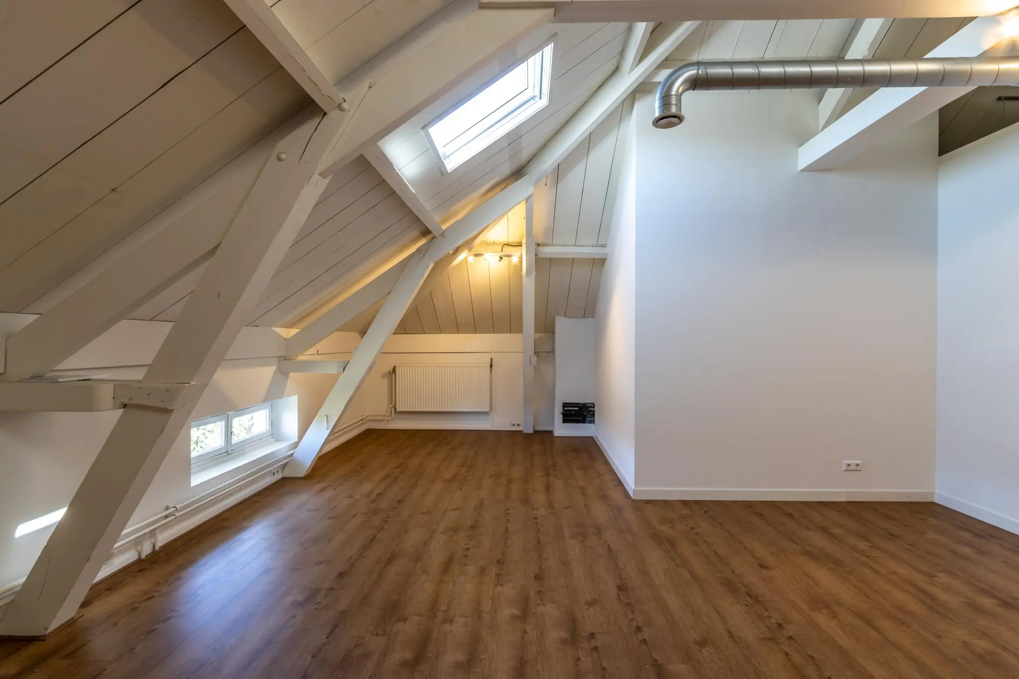 Zolderkamer aan de Utrechtseweg met schuine witte balken, houten vloer en dakraam.