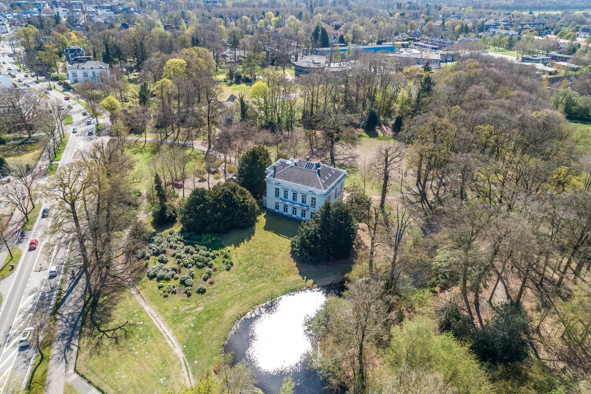 Luchtfoto van een wit landhuis aan de Utrechtseweg in Arnhem, omgeven door bomen, een vijver en parkachtig landschap.