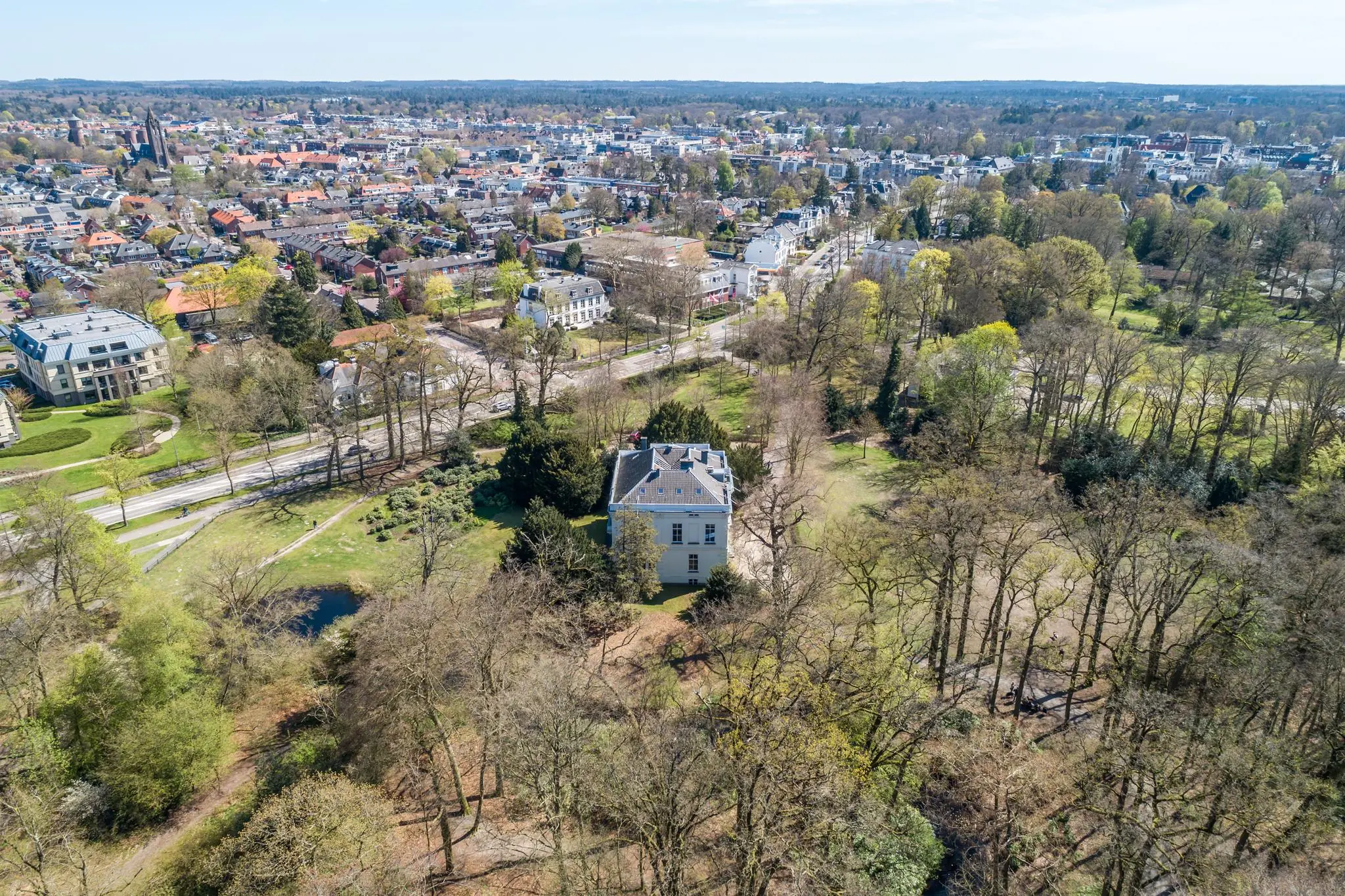 Luchtfoto van de Utrechtseweg in Arnhem met een wit landhuis omringd door bomen op de voorgrond en de stad op de achtergrond.