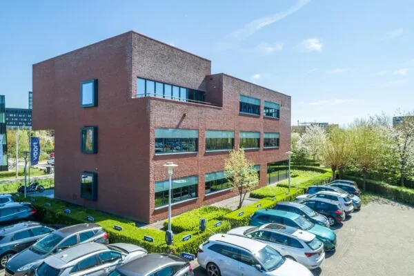 Modern kantoorgebouw aan de Groenewoudsedijk met parkeerplaatsen en omliggend groen.